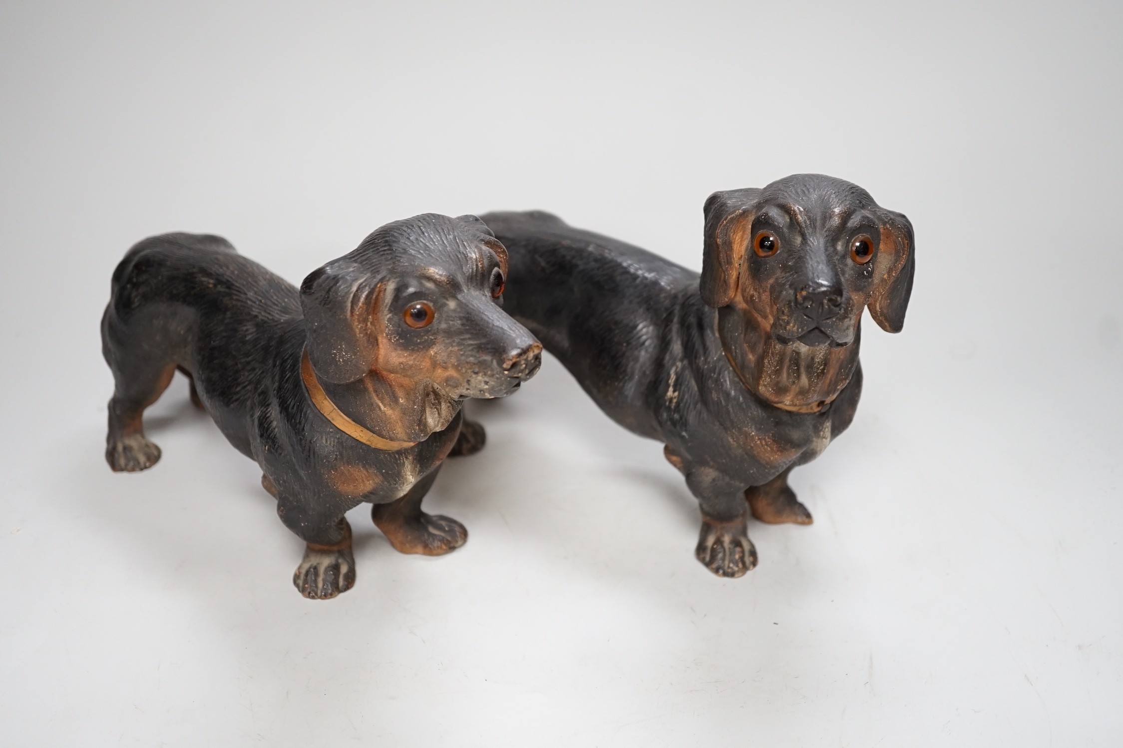 A pair of Austrian cold painted terracotta models of Dachshunds, one paw damaged, inset glass eyes 28cm long